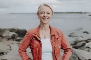 Dr. Tenna Dahl stellt sich lächelnd vor. Im Hintergrund sieht man das Meer und die Küste.